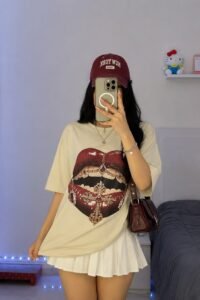 Blue oversized graphic tee styled with a soft neutral pleated skirt and casual sneakers