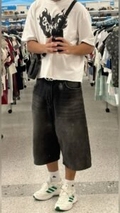 Streetwear college look featuring a white oversized graphic tee, dark jorts, and a shoulder bag